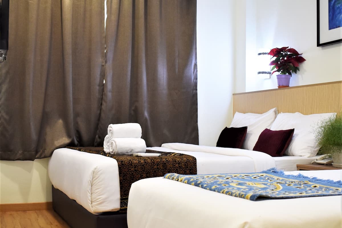 A hotel room with two beds, a large window with curtains, a bedside table with a plant, and a wall-mounted painting.