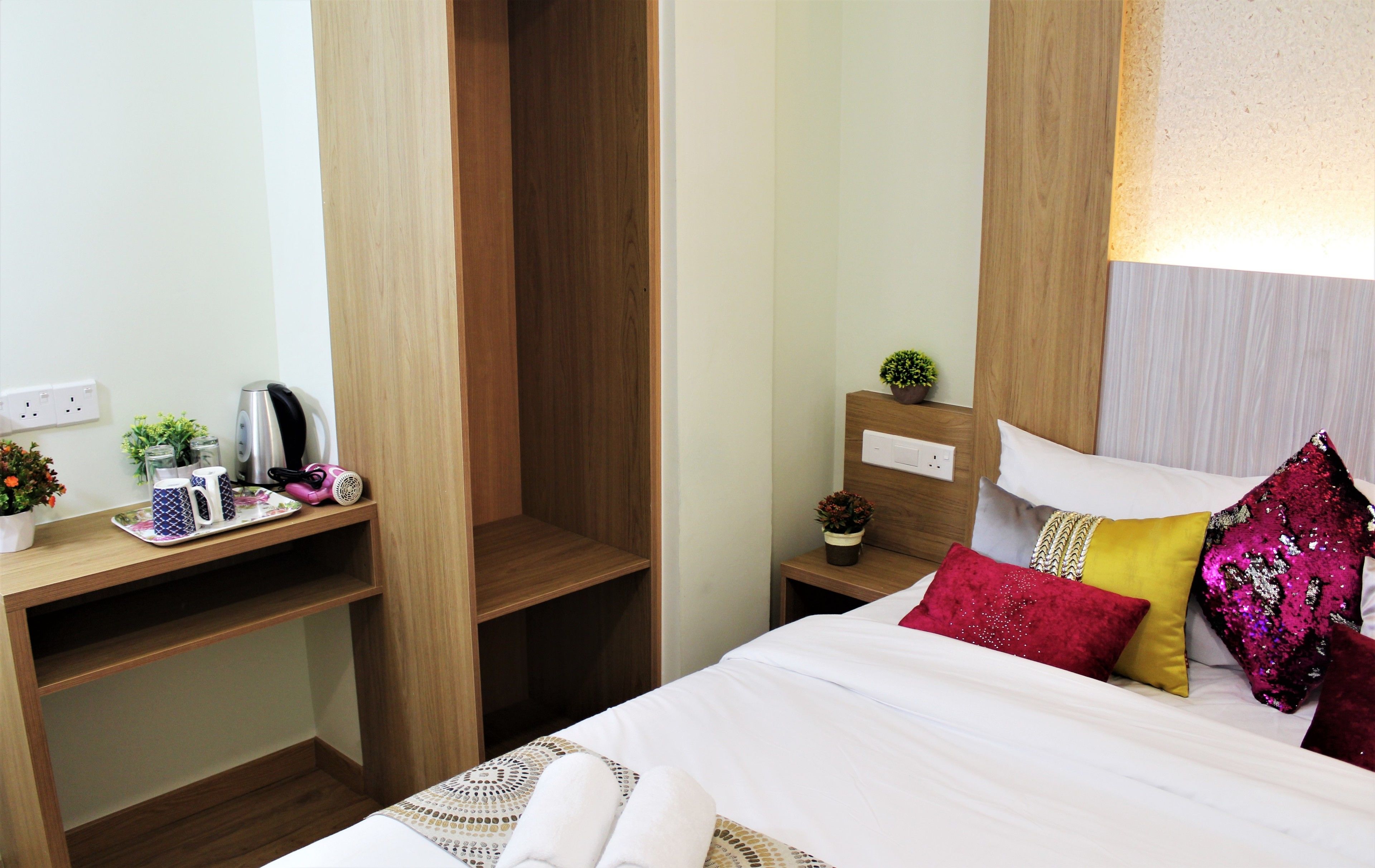 Una habitación de hotel con una cama, un escritorio de madera, una mesita de noche y una pequeña planta en maceta.