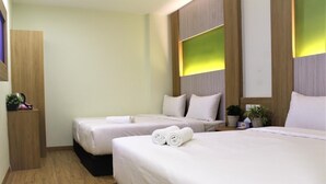 Quarto de hotel com duas camas, piso de madeira e uma pequena planta em uma prateleira.