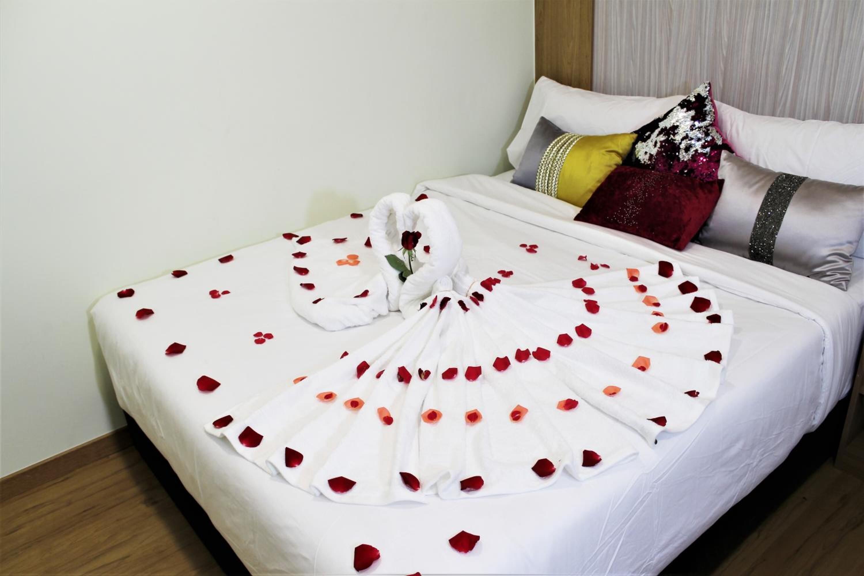 A neatly made bed with rose petals and a towel arranged in a fan shape.