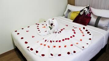 A neatly made bed with rose petals and a towel arranged in a fan shape.