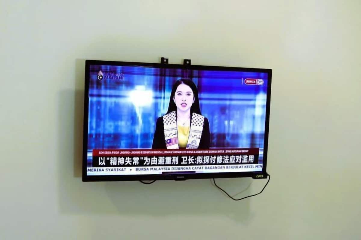 A television mounted on a wall displaying a news broadcast.