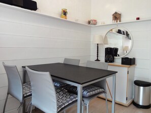 Ein gemütlicher Essbereich mit Tisch, Stühlen, einer Kaffeemaschine, einem Spiegel und einem Mülleimer.