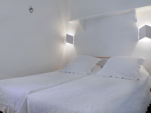 Una habitación pequeña y limpia con dos camas individuales, paredes blancas y un diseño sencillo y funcional.