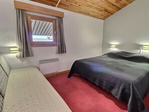 A small room with a bed, a window with curtains, a radiator, and two wall-mounted lights.