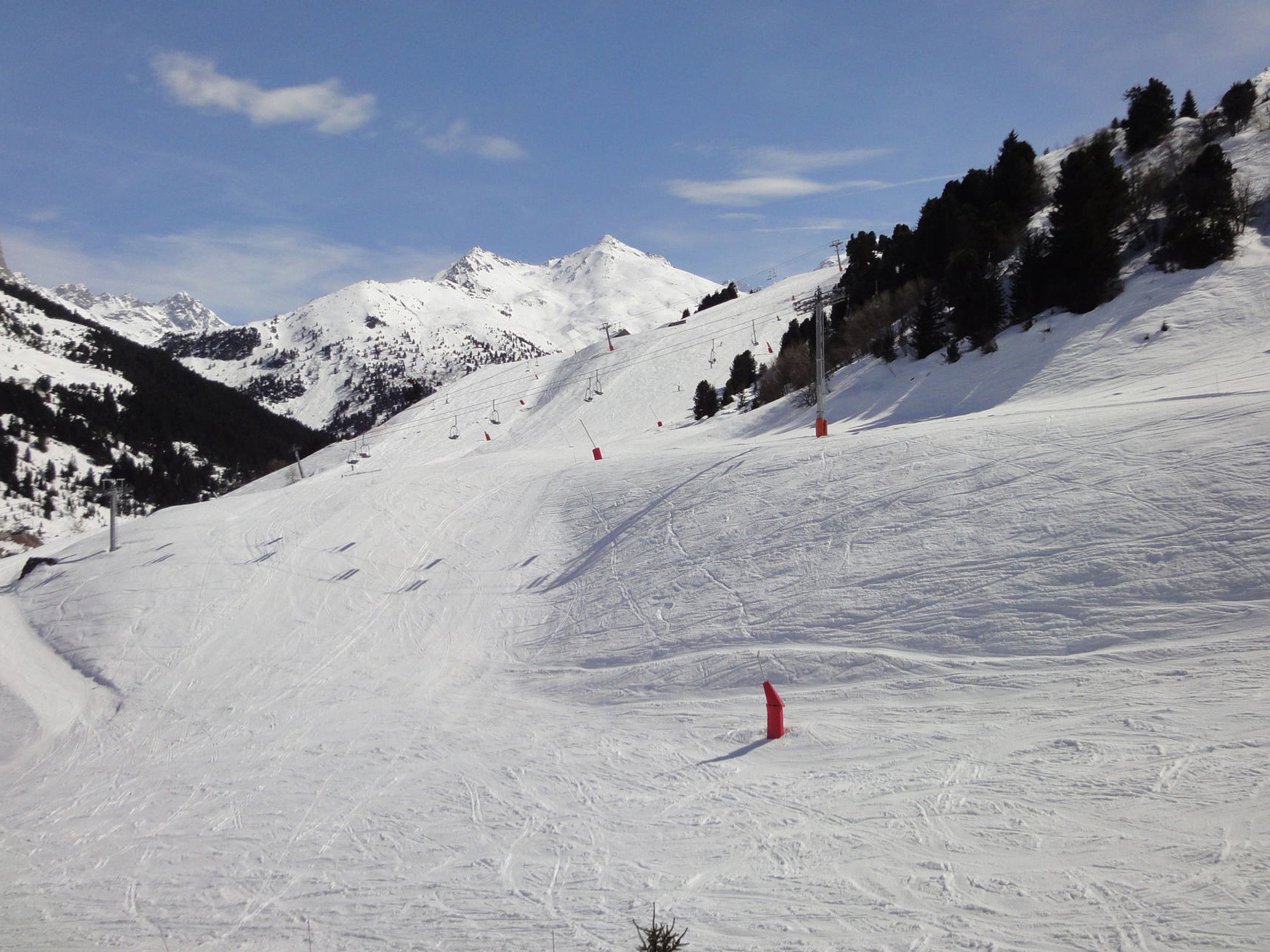 A snowy mountain slope with ski lifts, trees, and distant mountains.