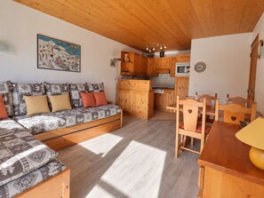 A cozy living area with a sofa, wooden dining table, and kitchen with wooden cabinets.