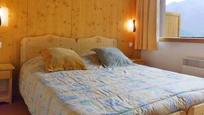 Habitación con paneles de madera, una cama, dos almohadas y ventana con vista a montañas.