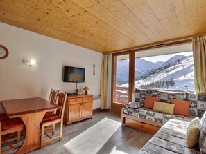 A cozy room with a wooden ceiling, a dining table with chairs, a sofa with patterned cushions, a flat-screen TV, and a view of snow-covered mountains. - Charming Méribel Apartment 3* - Pets Allowed (Méribel)