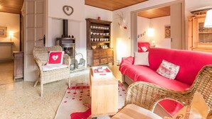 A cozy living room with a fireplace, wicker furniture, a red sofa, and a bookshelf. - 3-Room Apartment 6 Pers, Balconies, Pets Allowed, Near Shops (Le Monêtier-les-Bains)