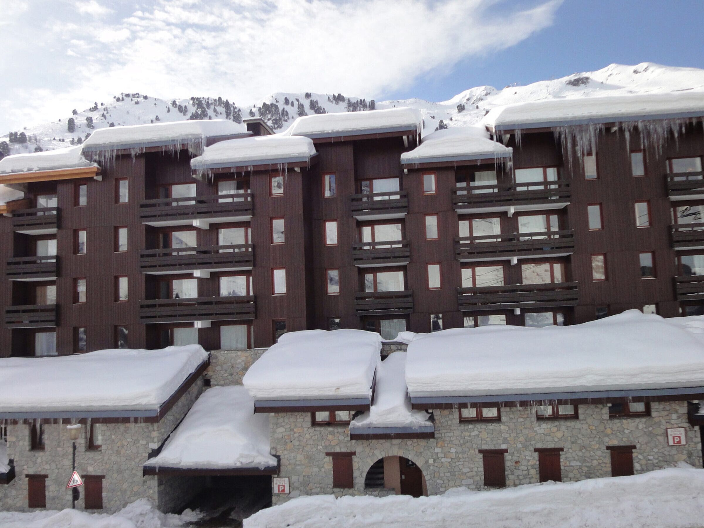 A multi-story hotel with snow-covered roofs and balconies, stone walls, and a mountainous backdrop.