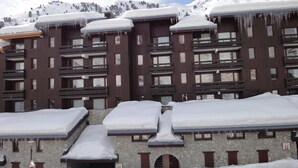 Ein mehrstöckiges Hotel mit schneebedeckten Dächern und Balkonen, Steinmauern und einer Bergkulisse.