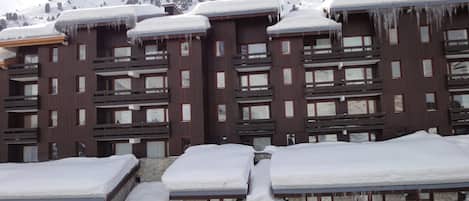 A multi-story hotel with snow-covered roofs and balconies, stone walls, and a mountainous backdrop.