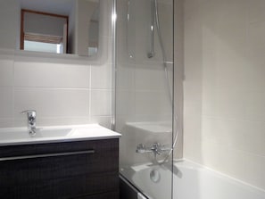 A modern bathroom with a glass shower enclosure, a white sink with a dark cabinet, and a mirror above the sink.