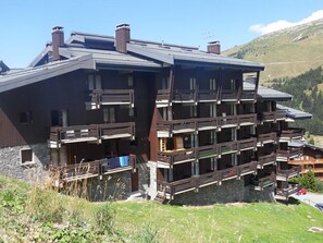 A multi-story chalet with balconies, set against a mountainous backdrop.