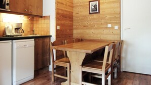 Eine Küche mit Holzschränken, einer Kaffeemaschine, einem Geschirrspüler und einem Esstisch mit Stühlen.