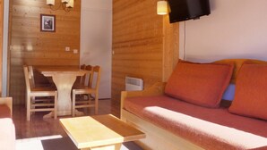 Ein Holzinnenraum mit einer Couch, einem Tisch, Stühlen, einem an der Wand befestigten Fernseher und einem Bilderrahmen.