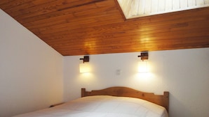 Ein Schlafzimmer mit Holzbalkendecke, zwei Wandleuchten und einem Bett mit weißer Bettdecke.