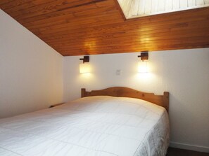 A bedroom with a wooden ceiling, two wall-mounted lights, and a bed with a white quilt. - Pleasant West Duplex Châtelet Area - Ideal for Family of 6 (Méribel)