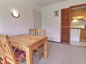 A dining area with a wooden table and chairs, a kitchen with wooden cabinets, and a door leading to another room. - Charming 1-Bed, Pets Allowed, Ski-in/Ski-out (Méribel)