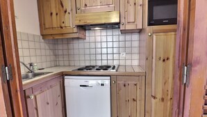 Ett kompakt kök med träskåp, en diskmaskin från Bosch, en mikrovågsugn från Samsung och en gasspis.