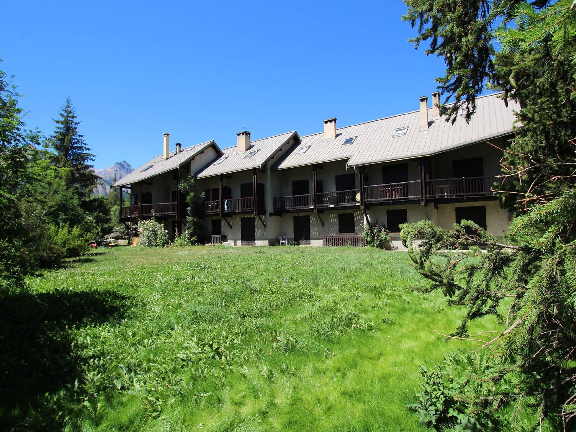 Un edificio de varios pisos con balcones, rodeado de exuberante vegetación y montañas al fondo.