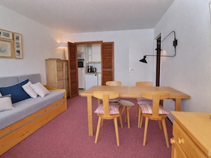 A compact living space with a sofa, a dining table with chairs, a kitchenette, and a lamp.
