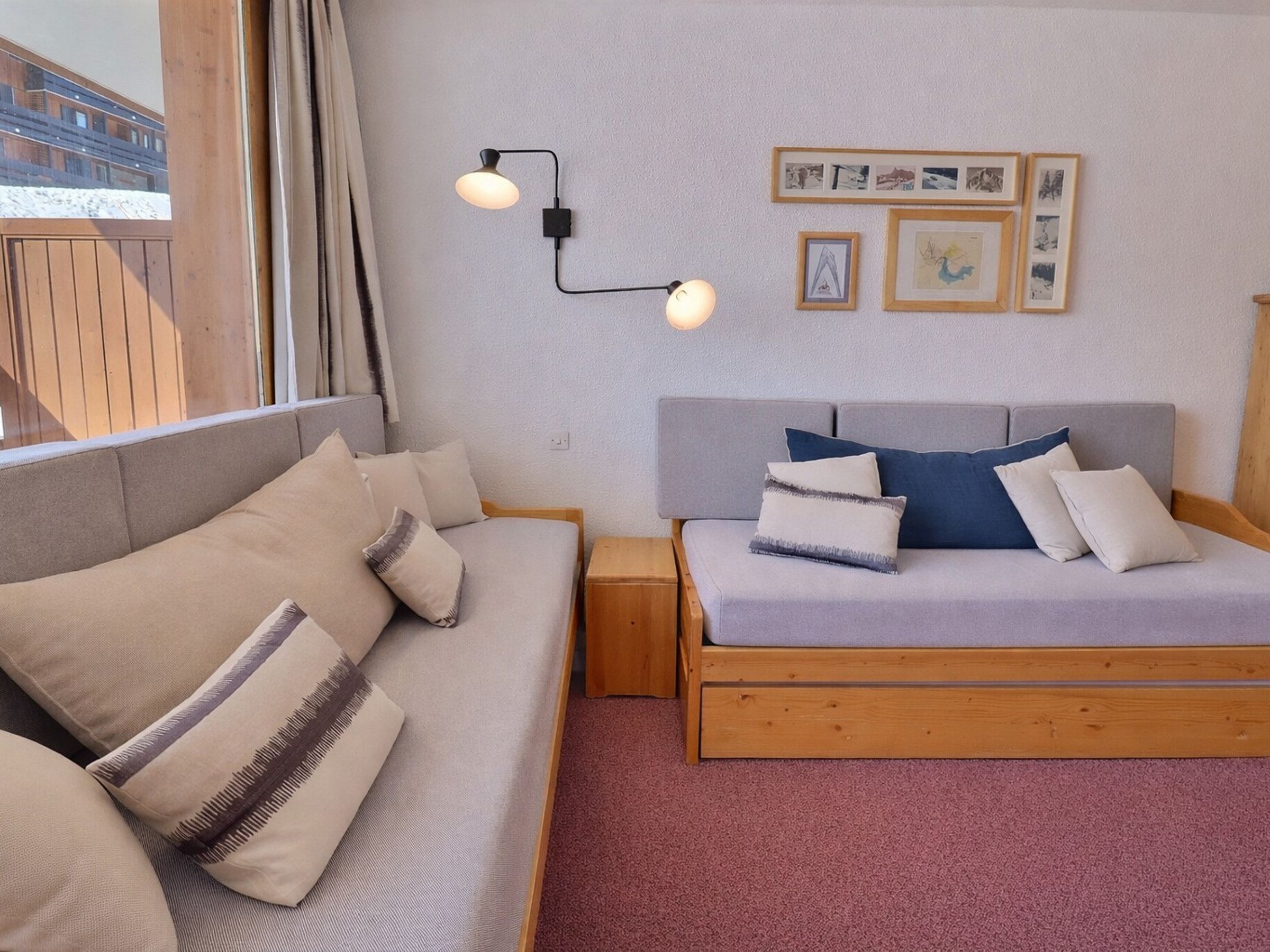 A room with a sofa, a bed, a nightstand, a wall-mounted lamp, and framed pictures.