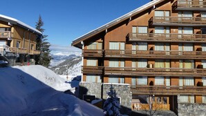 Un hôtel en bois à plusieurs étages, doté de balcons, qui se dresse sur fond de montagnes enneigées.