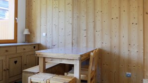 Een kamer met houten lambrisering, een tafel met stoelen, een raam en een aan de muur bevestigde televisie.