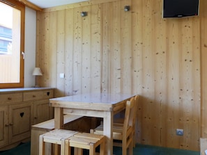 Une pièce aux murs lambrés, avec une table, des chaises, une fenêtre et un téléviseur fixé au mur.