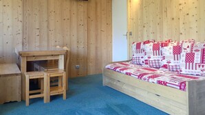 Een gezellige kamer met een houten wand, een bed met een rood-witte quilt, een klein houten tafeltje en een aan de muur bevestigde televisie.