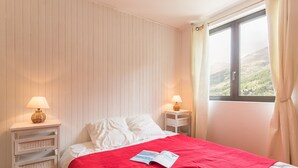 Ein Schlafzimmer mit einem Bett, zwei Nachttischen, einem Fenster mit Vorhängen und Blick auf eine Landschaft.
