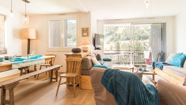 Ein gemütliches Wohnzimmer mit einem Holzesstisch, einer Couch und einem Balkon mit Blick auf die Landschaft.