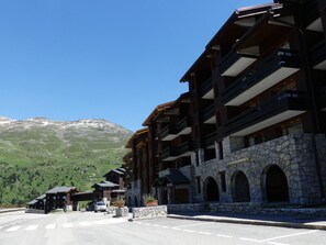 Hotel de vários andares com fachada de pedra e varandas, com montanhas ao fundo.