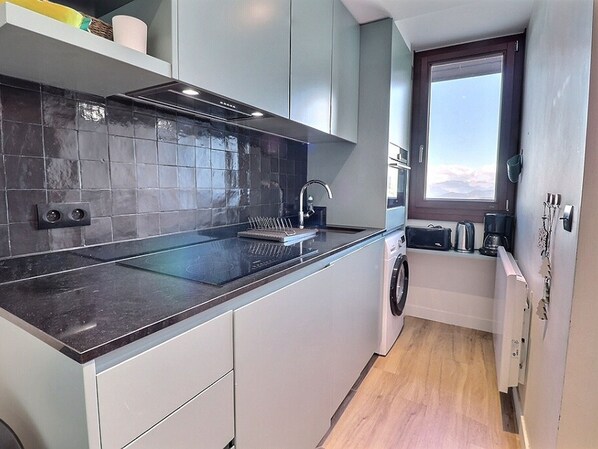 A modern kitchen with a black countertop, grey cabinets, and a window with a view.