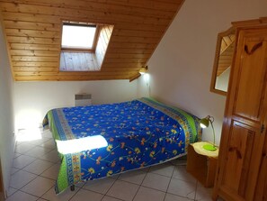 A bedroom with a sloped ceiling, a skylight, a bed with a floral bedspread, a bedside table with a lamp, and a wooden wardrobe. - Spacious 3-Room Apartment for 5, Near Serre Chevalier Ski Area (La Salle-les-Alpes)