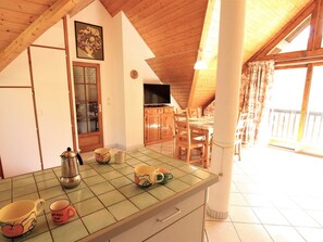 Uma cozinha com bancada em azulejo, armários de madeira e um espaço de jantar com cadeiras e mesa.