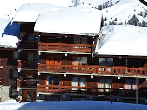 A multi-story wooden building with balconies, surrounded by snow-covered mountains.