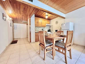 Un comedor con una mesa y sillas de madera, una cocina al fondo y un refrigerador blanco.