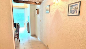 Un pasillo con piso de baldosas, una silla de madera, una mesita y una puerta que da a un área exterior.