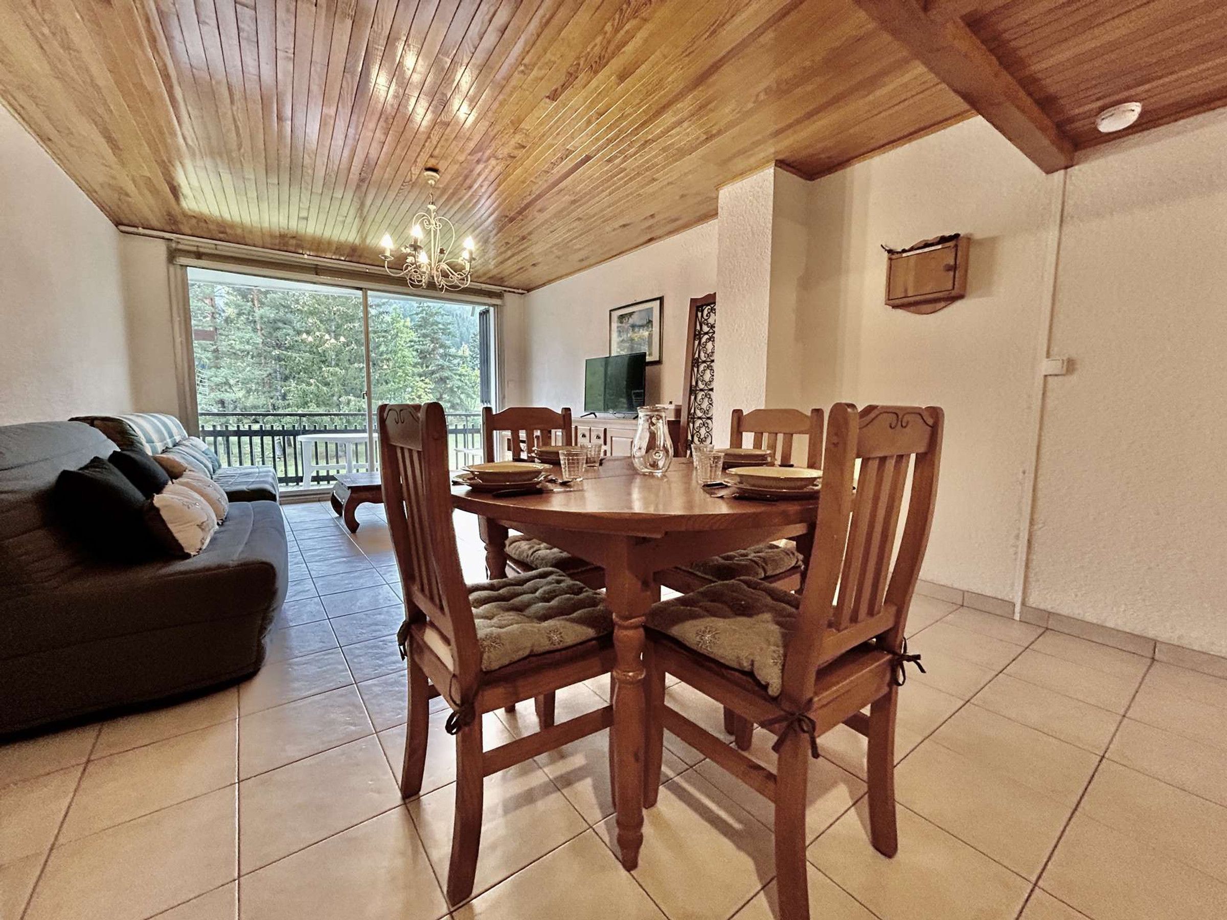 Un comedor con una mesa y sillas de madera, un sofá y un televisor al fondo.