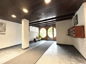 A hallway with a stone column, a wooden bench, and a door with circular windows.