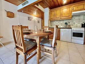 A dining area with a wooden table and chairs, a kitchen with wooden cabinets and appliances, and a tiled floor.