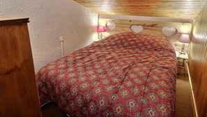 Ein Schlafzimmer mit Holzboden, einem Bett mit rot gemustertem Bettbezug und herzförmigen Wanddekorationen.