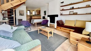 A cozy living room with a sofa, chairs, a coffee table, and a fireplace. There is a kitchen in the background.