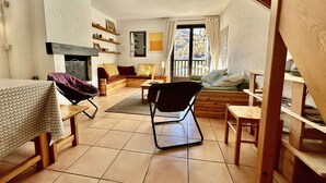 A cozy living room with a fireplace, a sofa, a dining table, and a chair.