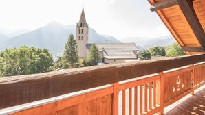 A wooden balcony with a view of a church and mountains.