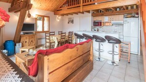 A cozy cabin with a wooden interior, a dining area with a table and chairs, a kitchen with a refrigerator and microwave, and a loft bedroom with a wooden bed.