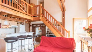 A spacious living area with a wooden staircase, a red sofa, and a kitchen in the background.